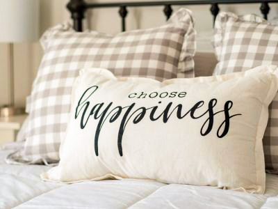 Två rutiga kuddar och en med texten "choose happiness" fint ställda i en säng efter städning i Stockholm.